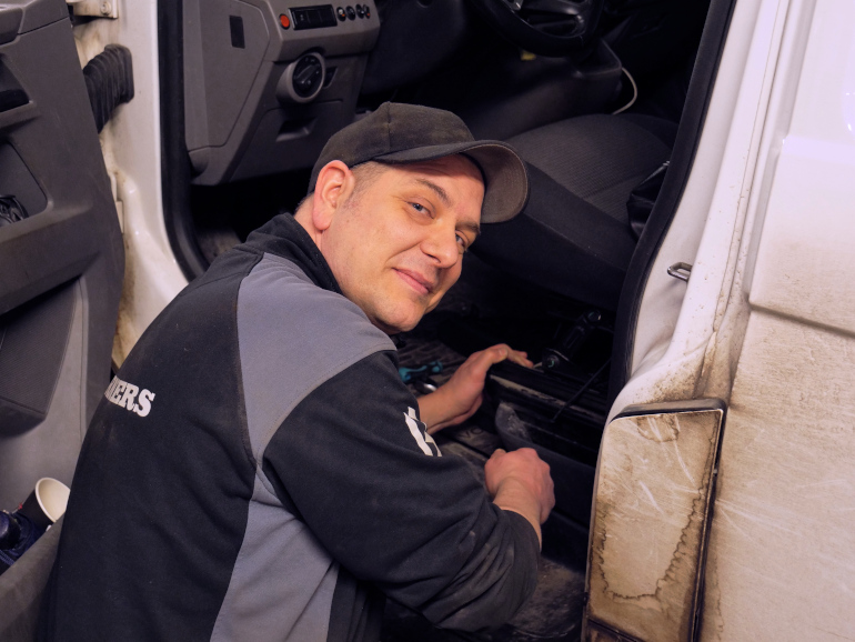 En person i keps och verkstadskläder justerar ett säte i en bil