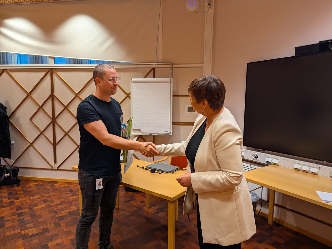 En person har fått en tulpan och ett diplom och skakar hand med en annan person