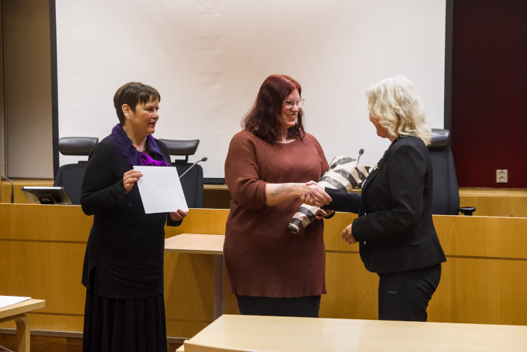 En person får en blomma av en annan person. En tredje person är förberedd att dela ut ett examensstipendium.