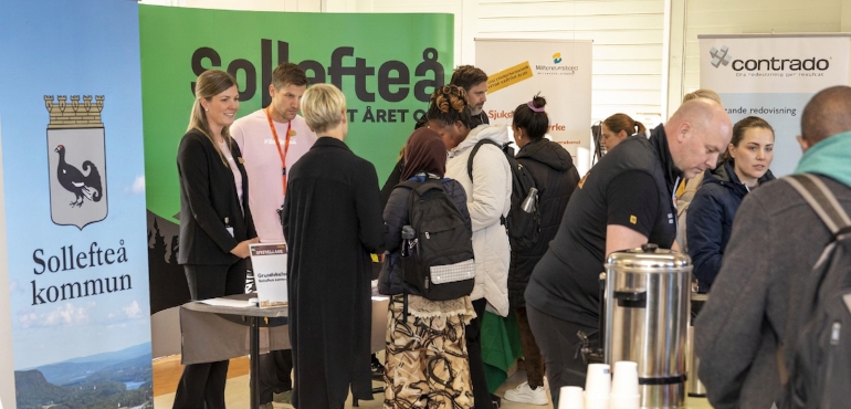 Mässbesökare framför montrar med olika rollups, i förgrunden serveras kaffe
