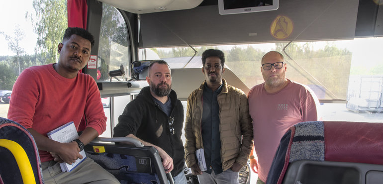 Fyra elever från yrkesförarutbildningen stående i en buss