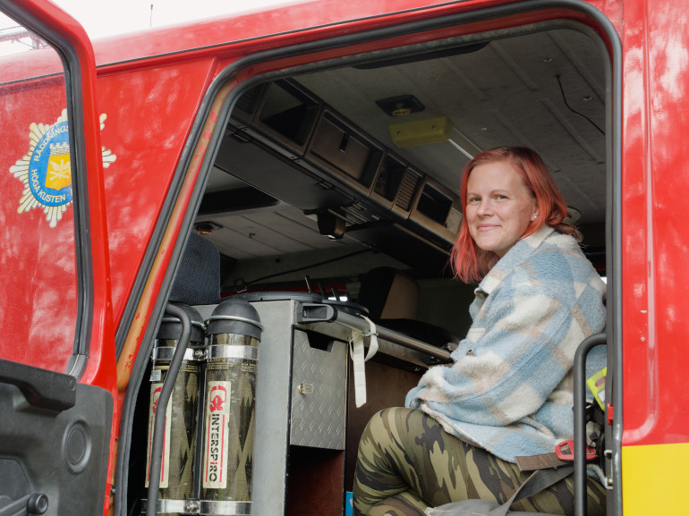 En kvinna med rött hår och en varm tröja sitter i en brandbil