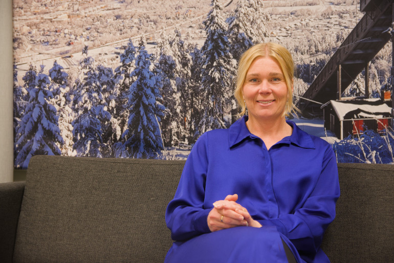 Portätt av kvinna i blå klänning framför tavla föreställande vinterlandskap