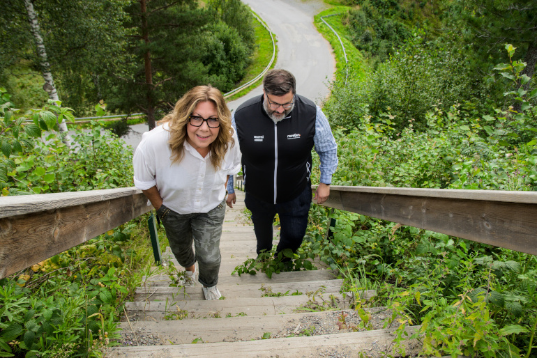 En kvinna och en man går upp för en trappa omgiven av gröna växter