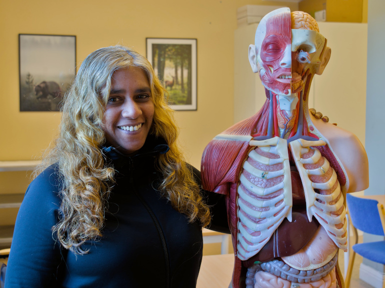 Kvinna står i klassrum bredvid en anatomisk modell